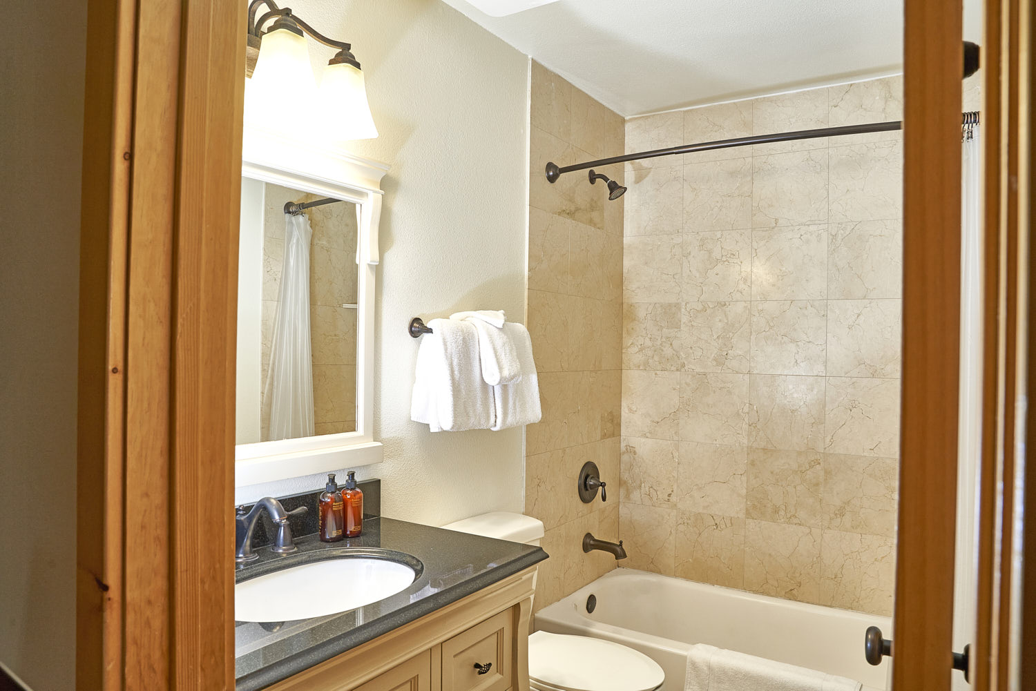 Bathroom with marble finish, corner bathtub, towel on iron rod, mirror above washbasin.