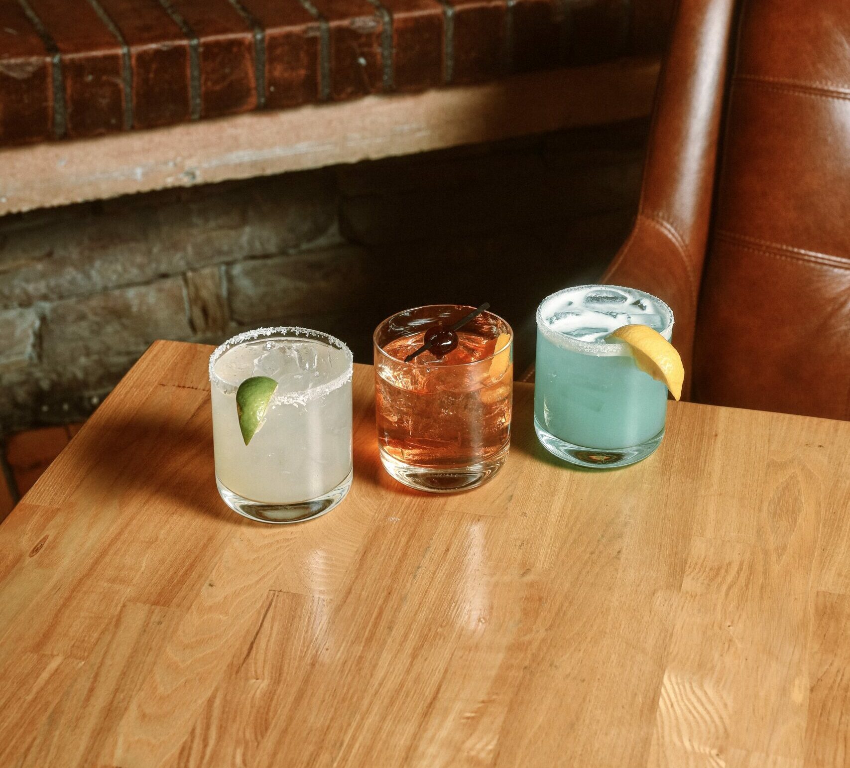 Three distinct cocktail glasses elegantly arranged on the edge of the wooden finish table.