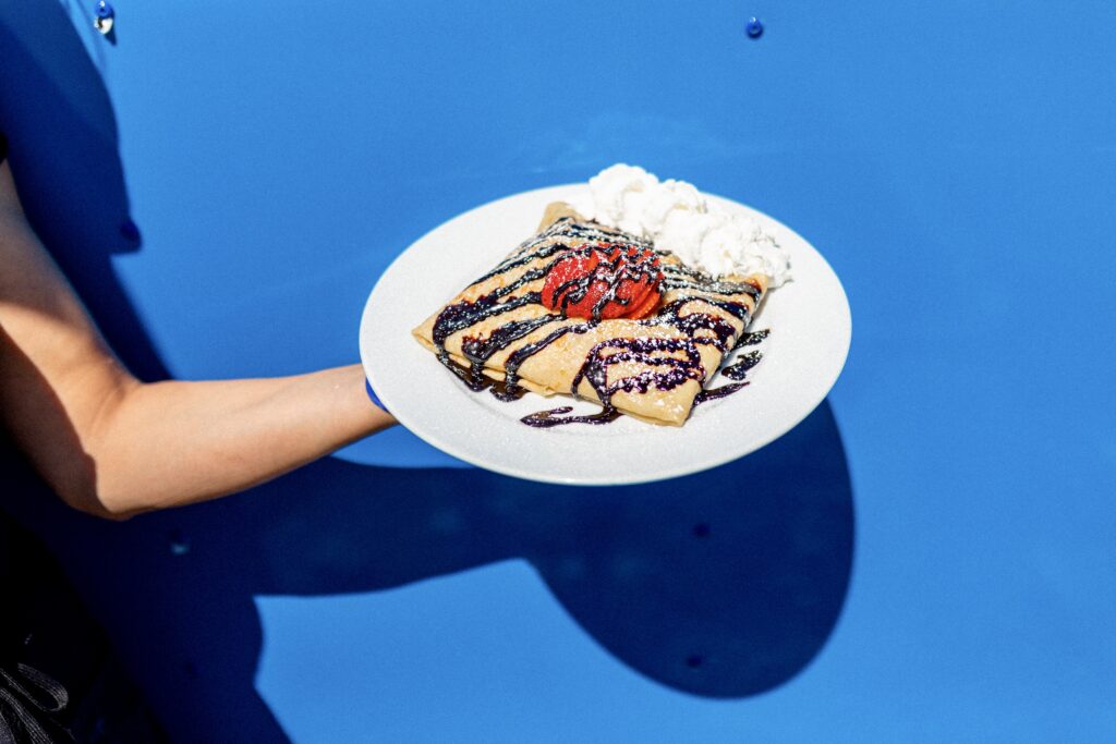 Hand showcasing a plate of delectable food against a backdrop of a blue wall.