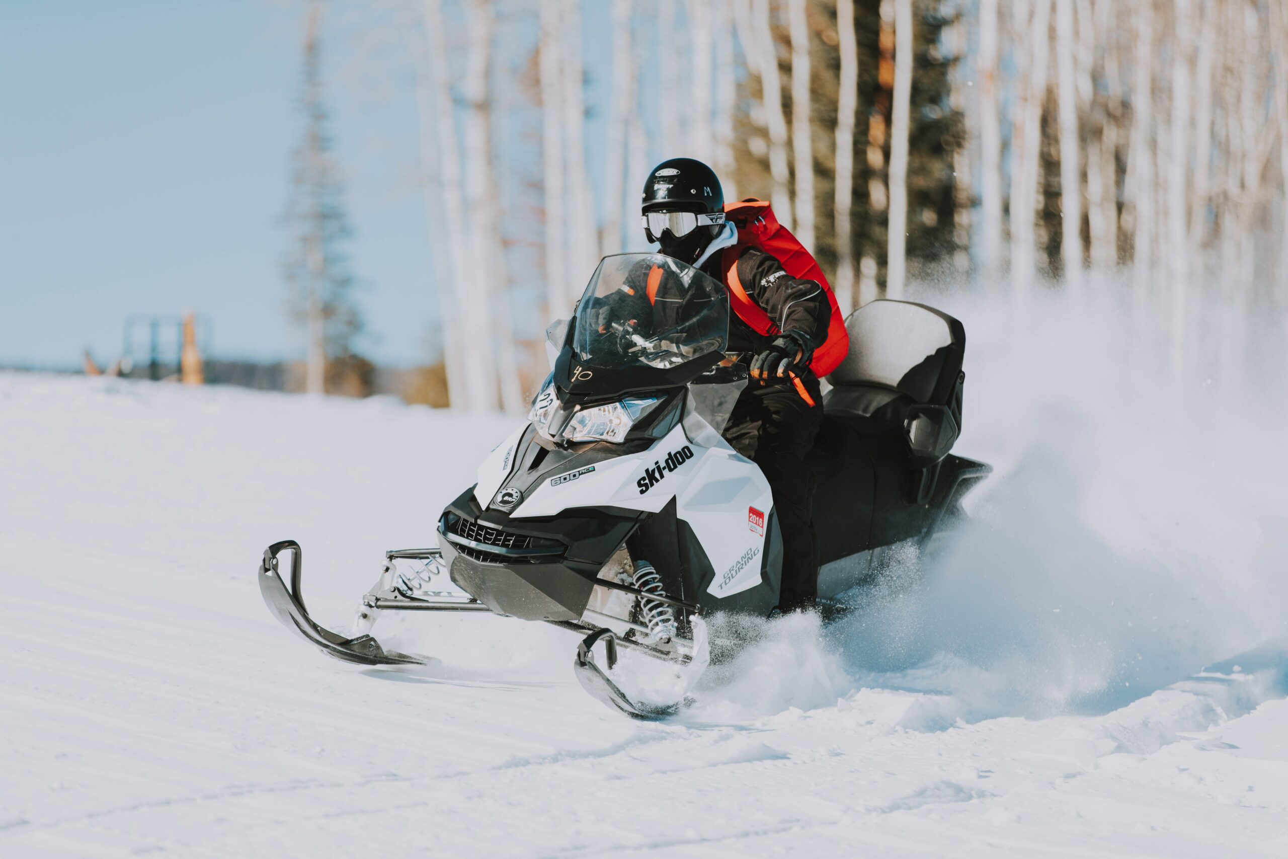 A man maneuvers a Ski-Doo snow bike through dense trees on a snowy mountain.