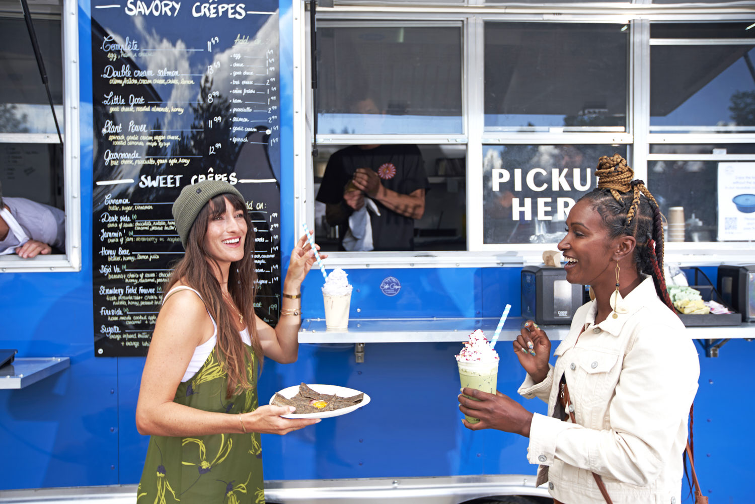 Two women relishing a meal and drinks, standing at the food truck.