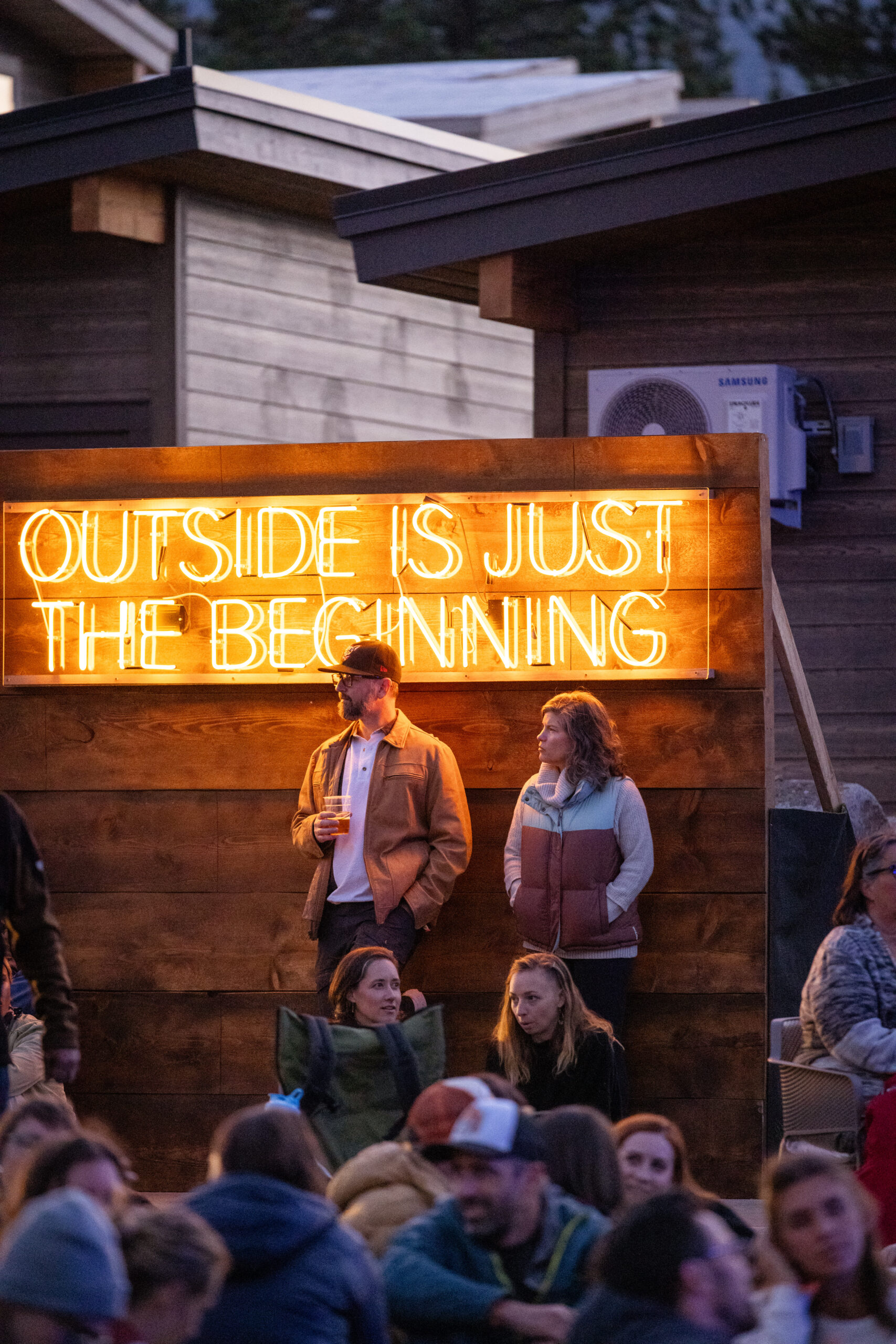 A couple stands apart from the crowd under a signboard that reads "Outside is just the beginning."