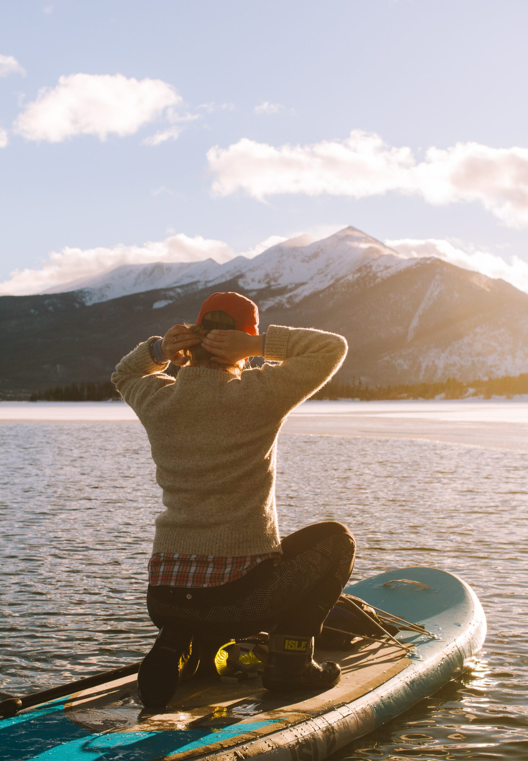 A woman on a paddleboard at sea, admiring the sunrise over snowy mountains.