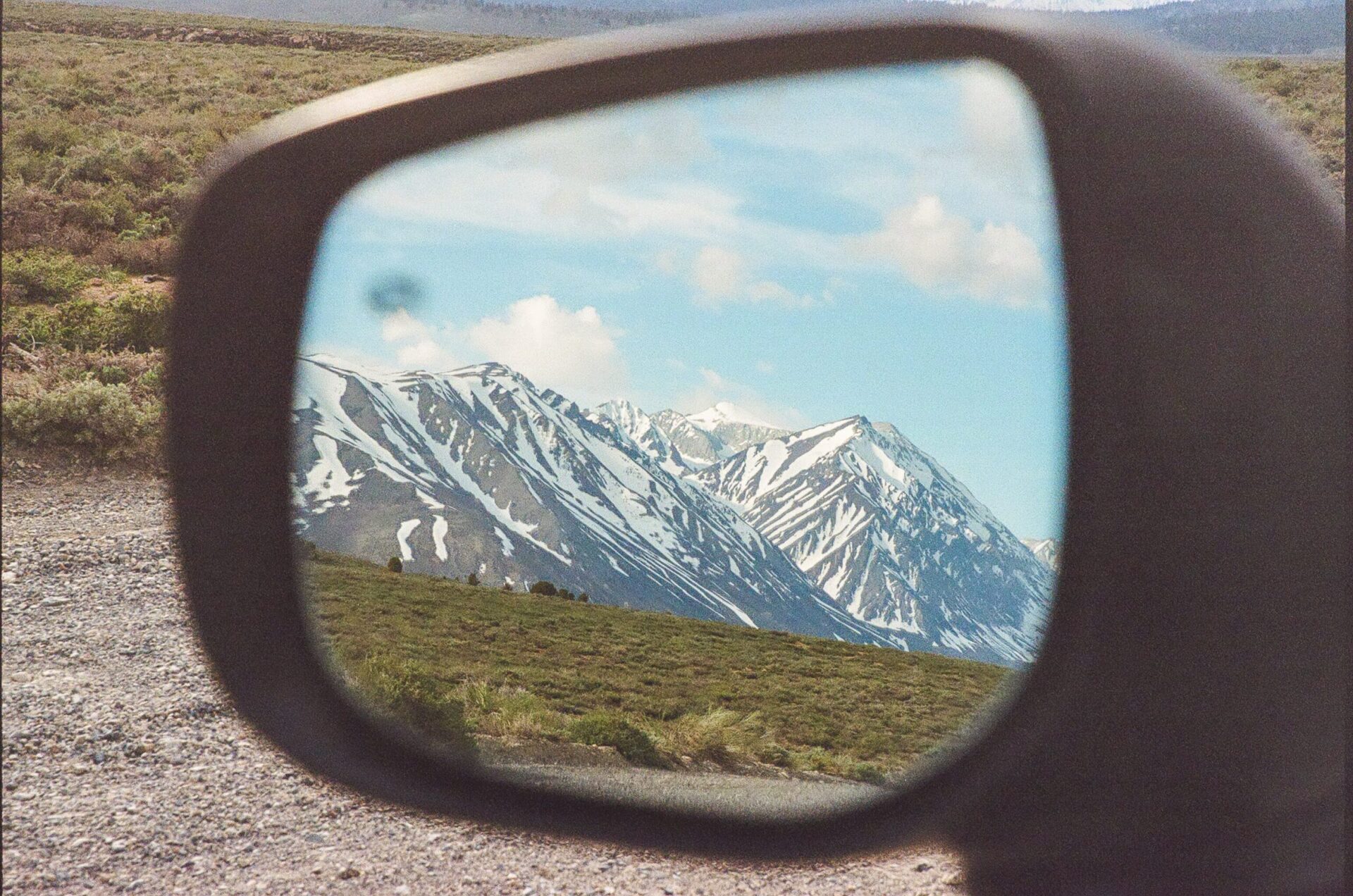 The car's side mirror reveals a spectacular snowy mountain view, creating an enchanting scene.