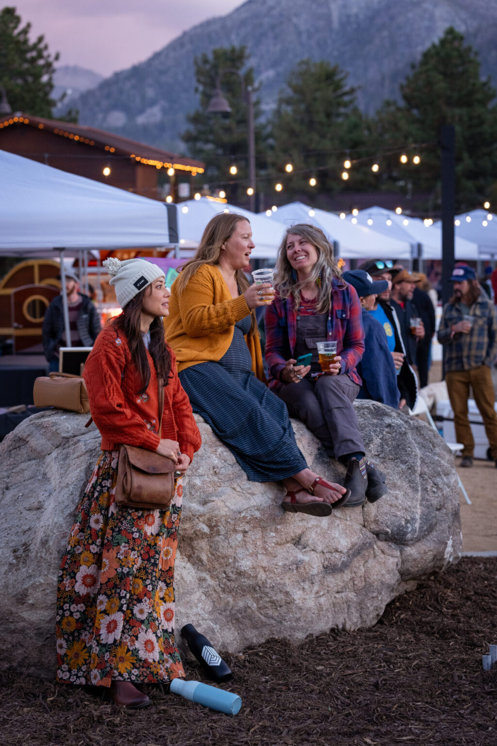 Three girls seated on a rock, two sipping wine, one savoring the evening view.