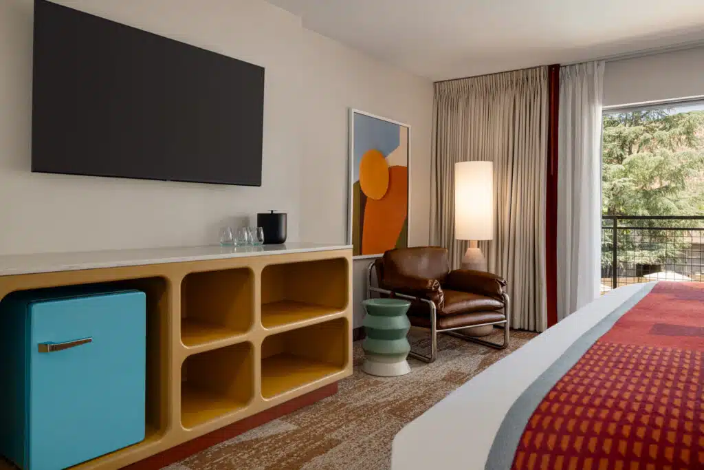 A hotel room with a large bed, TV, mini-fridge, and sitting area.