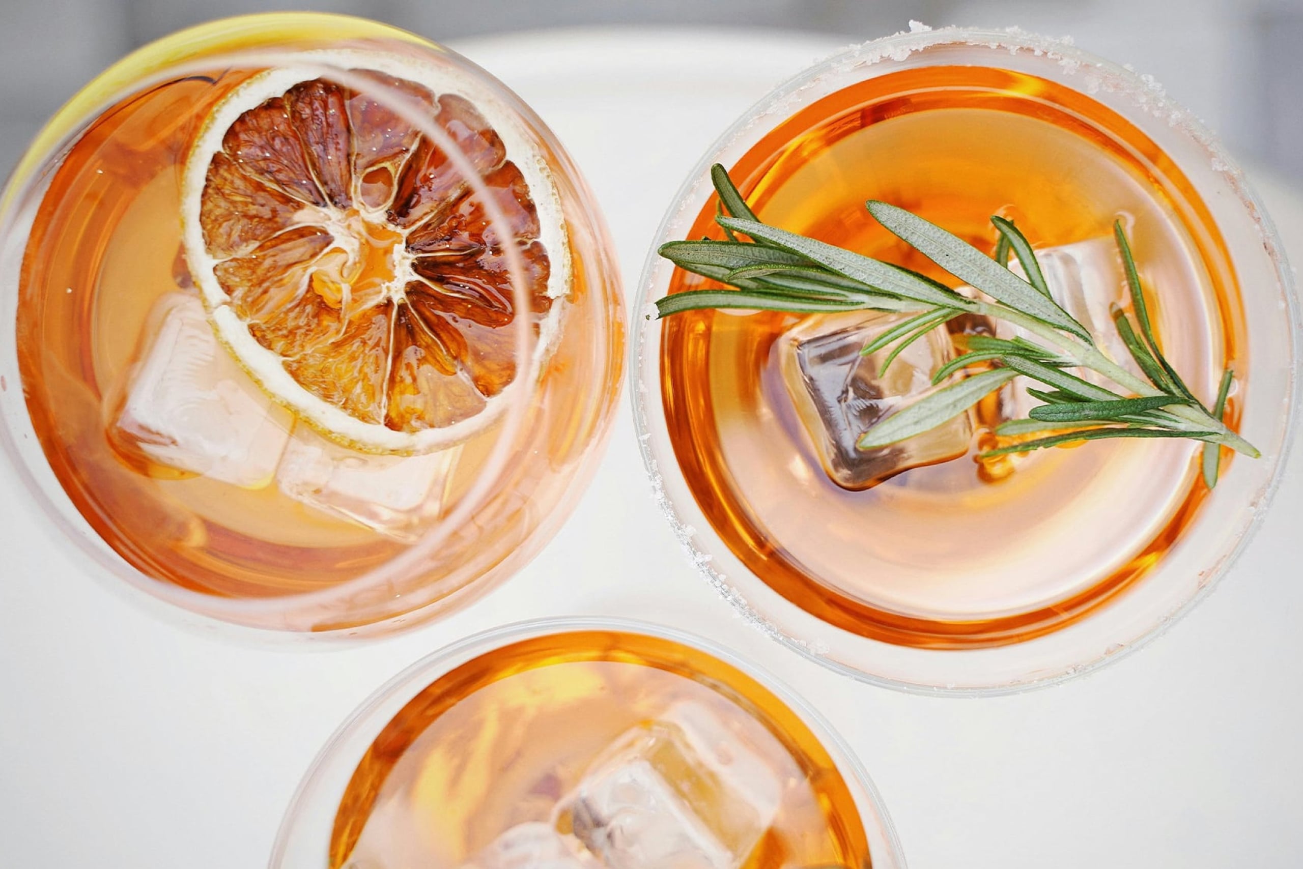 three glasses of orange liquid with ice cubes and garnishes