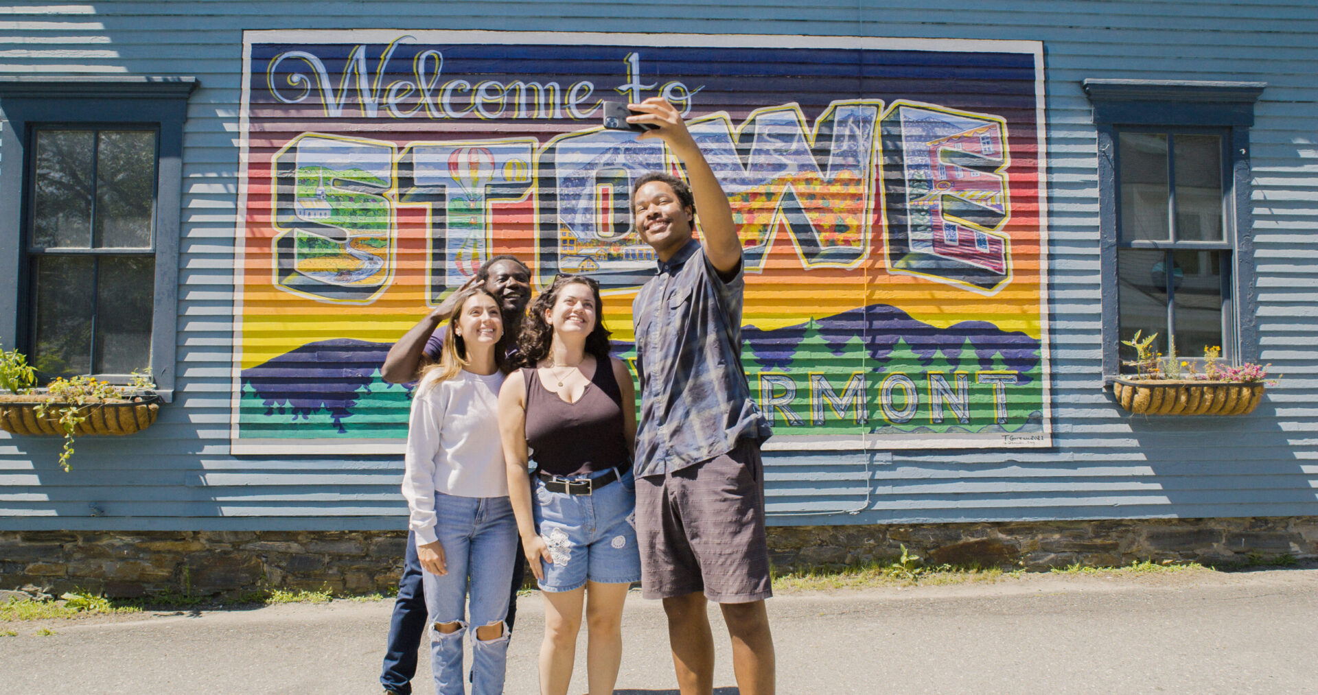 Group taking a selfie in front of Welcome To Stowe, Vermont mural near Outbound Hotels nature hotel in VT