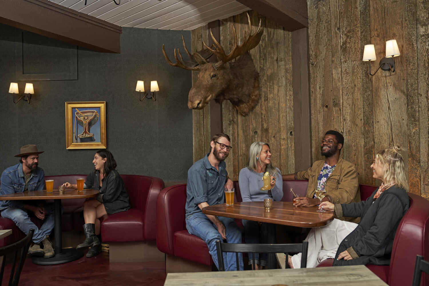 Cozy sofas host people enjoying drinks, complemented by a handcrafted Moose head on the wall.