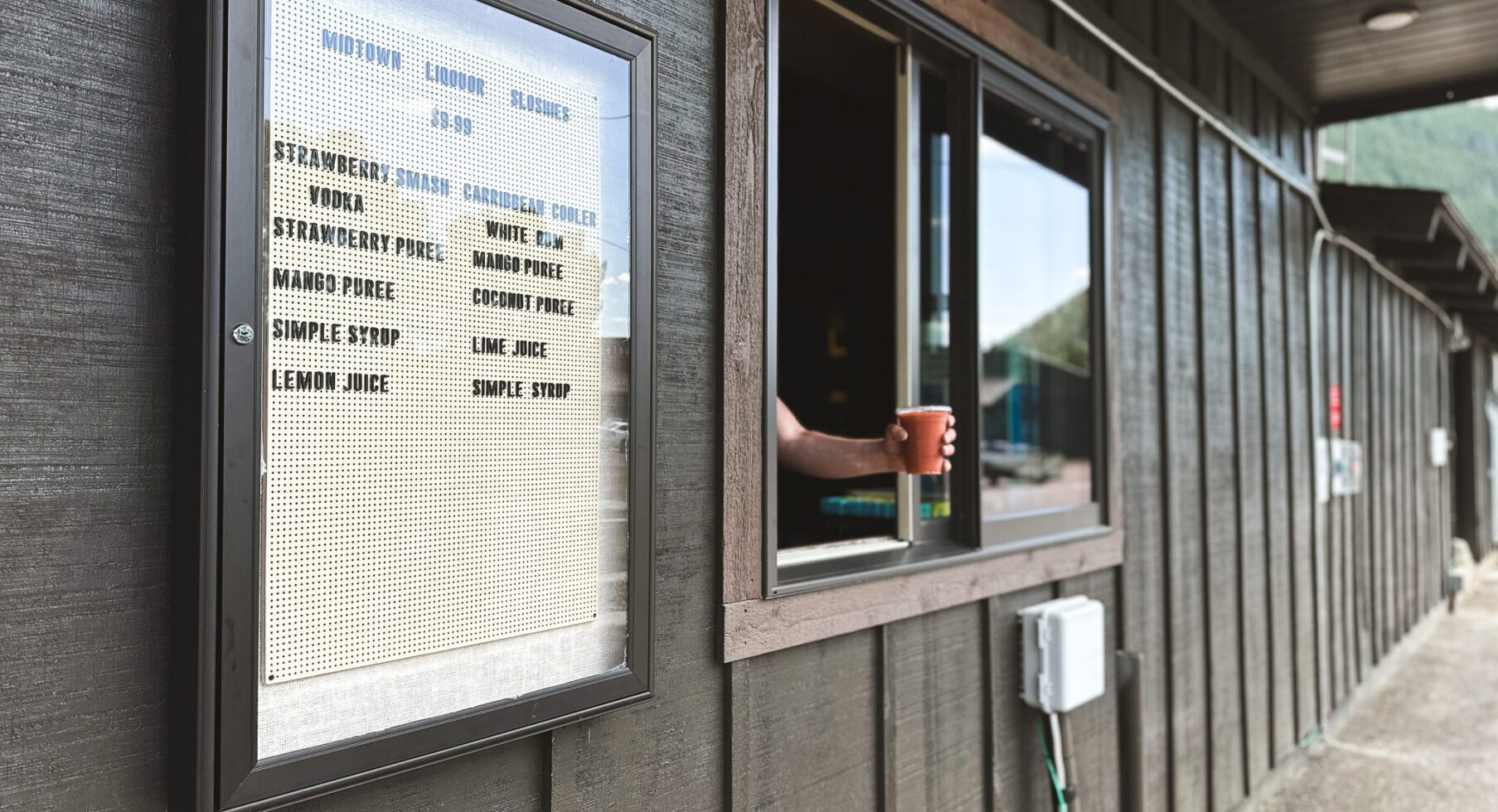 From the counter window, a hand holding a coffee mug is visible, with a nearby menu card.