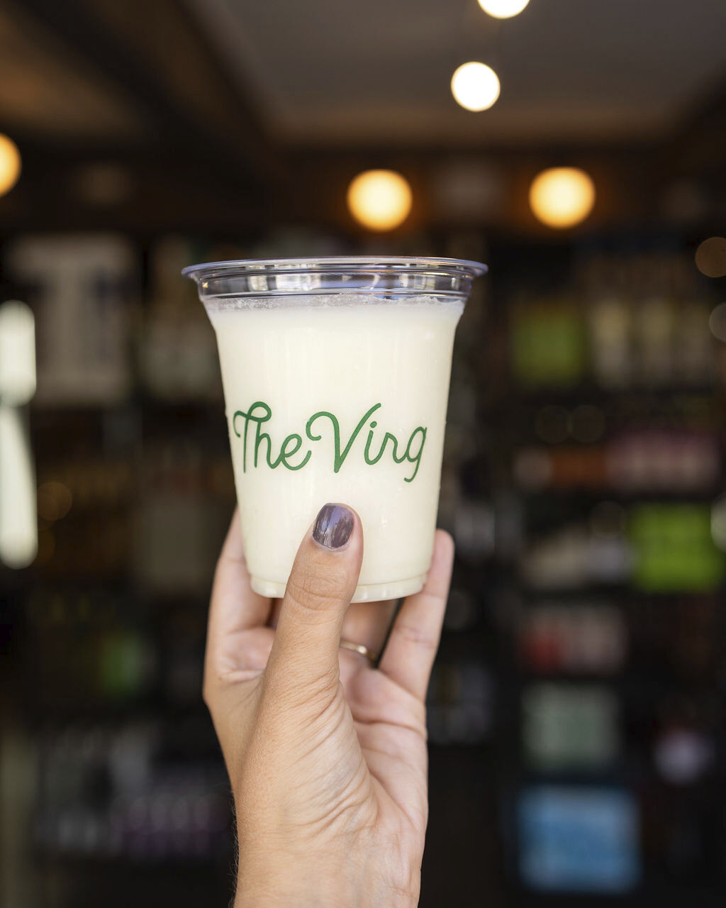 A photo captures a hand holding a juice glass featuring "The Virg" logo.