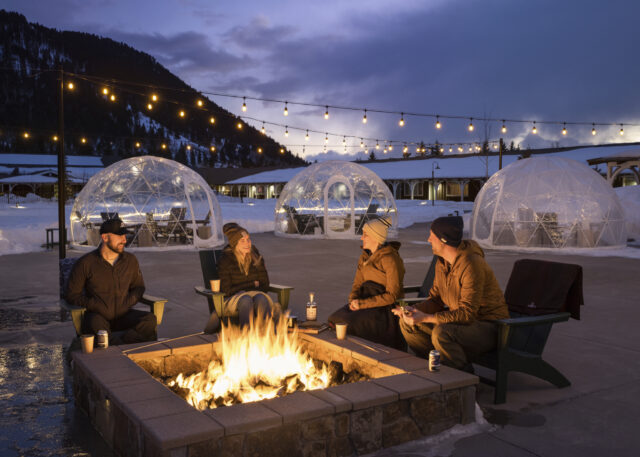 Seated by the bonfire, people enjoy conversation with an awesome evening sky view.