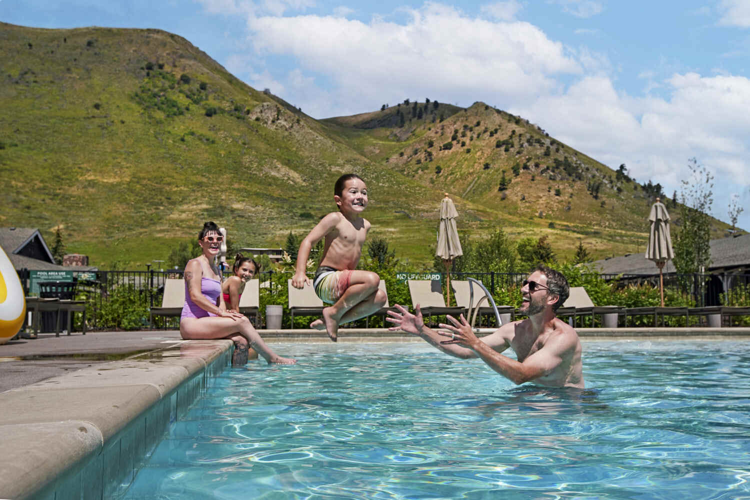 Family enjoys memorable moments in the pool, embracing a delightful view of lush green mountains.