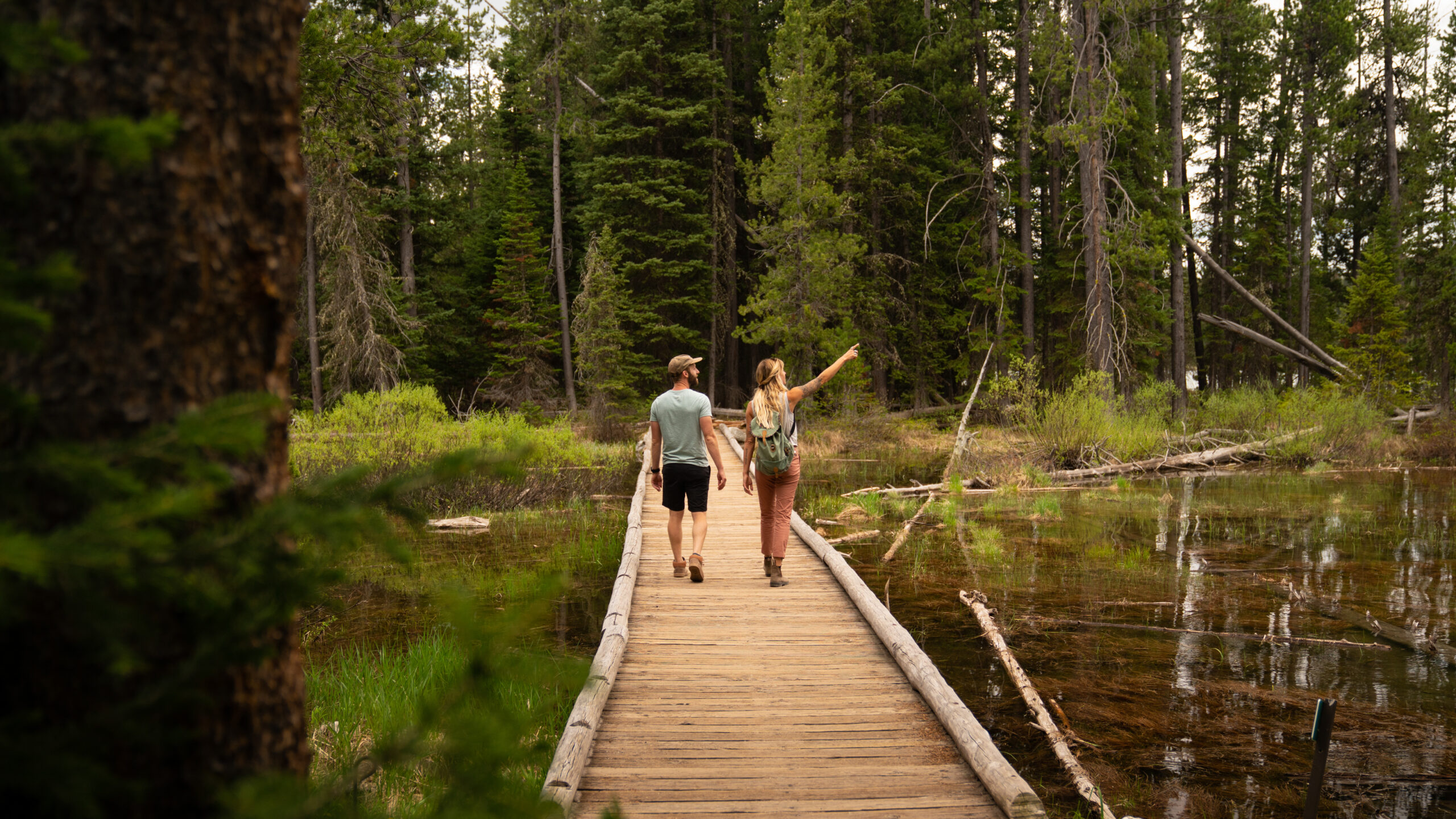 A guy and a girl traveling on a ranch by the pond, admiring the green forest scenery.