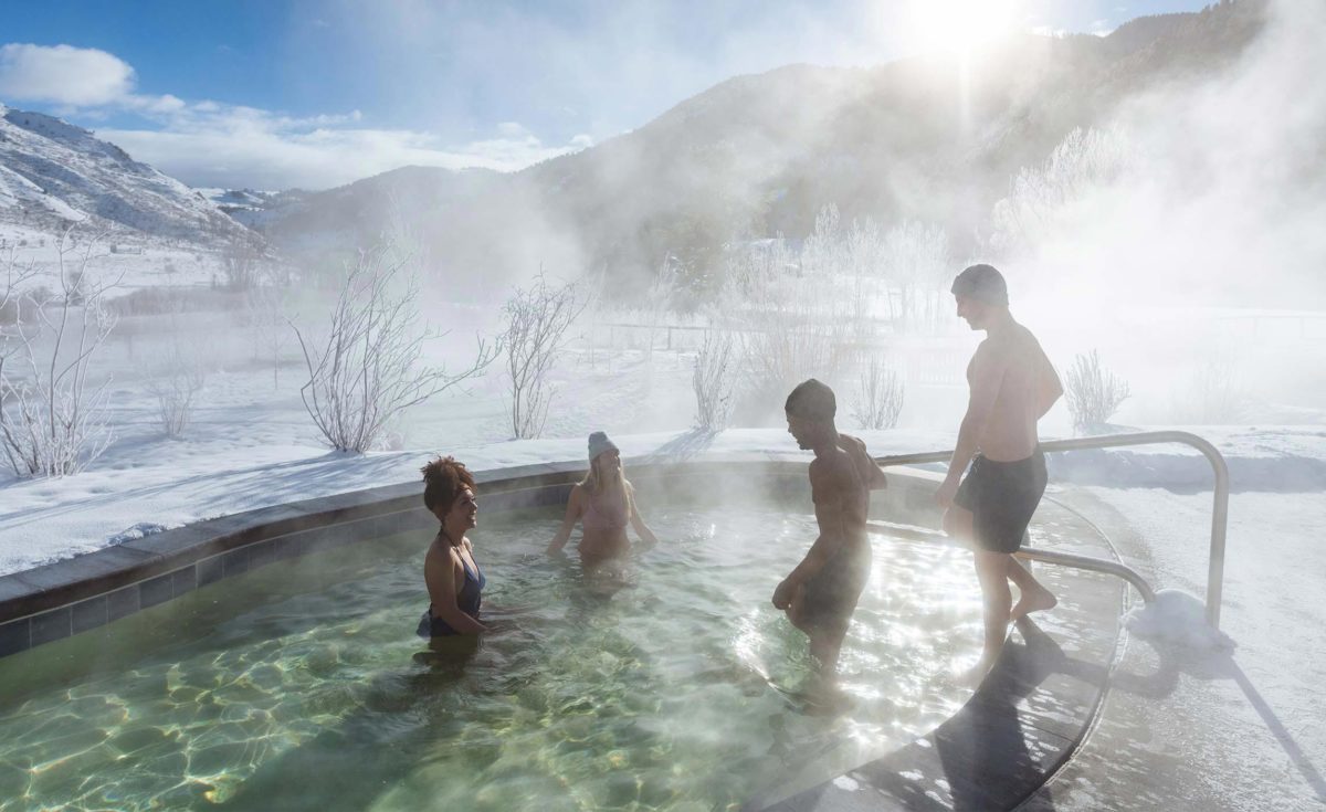 In a hot water swimming pool, people enjoy a stunning view of snowy mountains.