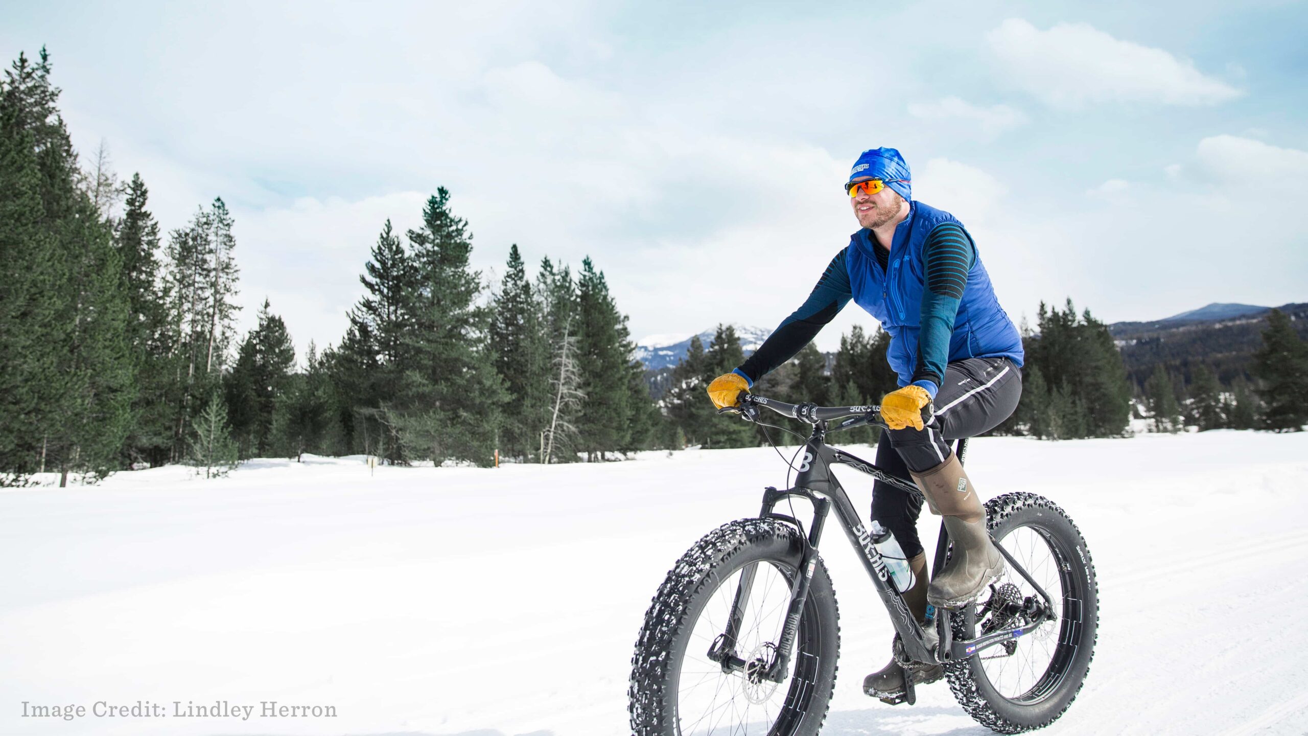 A man cycles his fat bike through thick snow, enjoying a splendid mountain view.