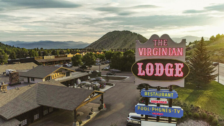 Drone captures "The Virginian Lodge" exterior with a stunning view of lush greenery mountains.