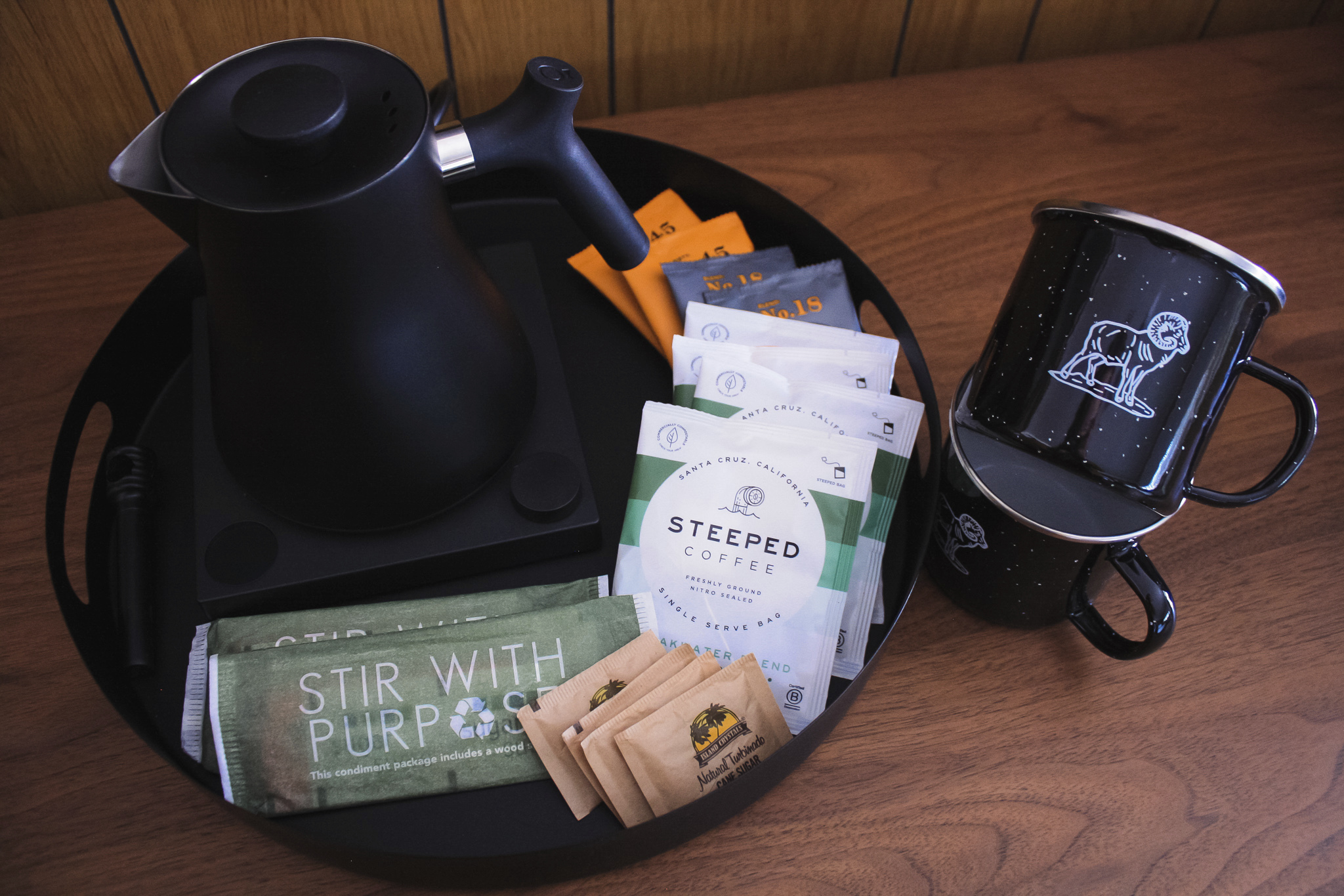 A stunning black kettle pairs with a coffee cup, accompanied by stepped coffee and sugar pouches.