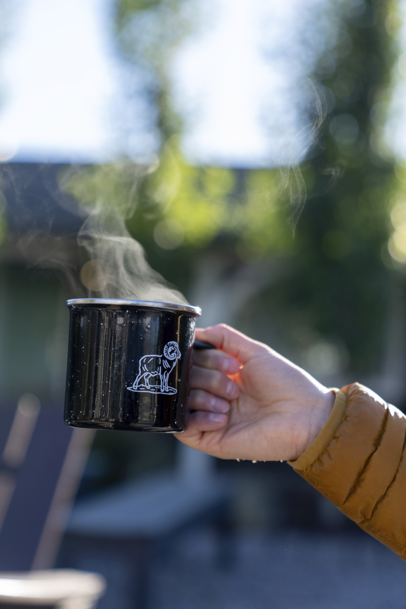 A hand grips a coffee mug, adorned with a longhorn mountain goat logo.