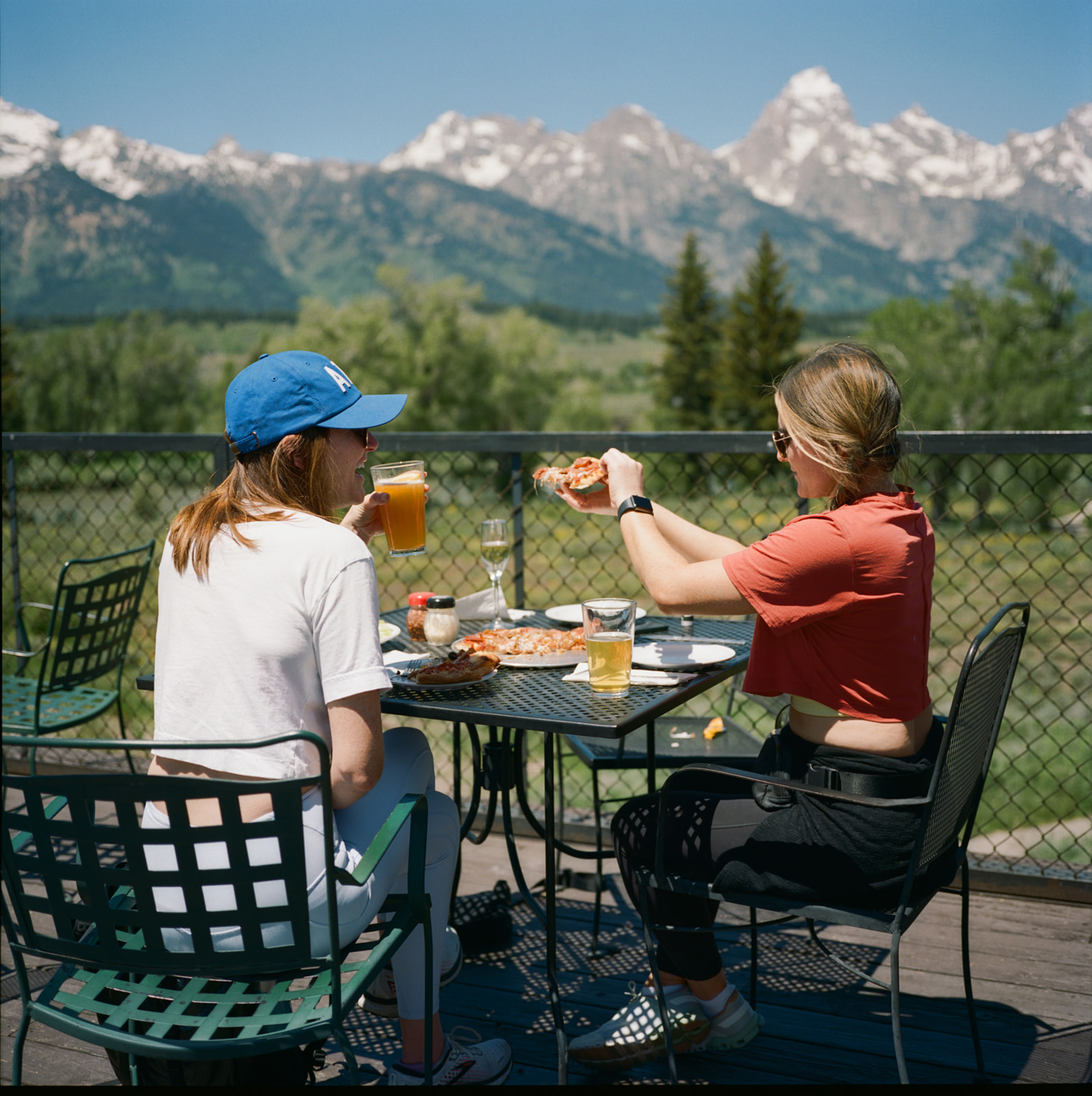 Girls savoring breakfast and cocktails, relishing a wonderful view of trees by the mountain.