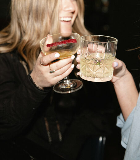 Girl cheerfully raises her alcohol glass, sharing smiles with others in celebration.