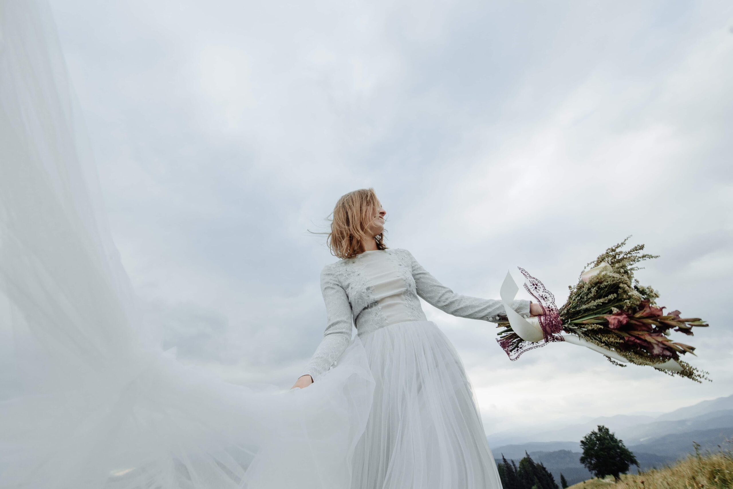 A bride in her wedding gown happily enjoys the moment, holding a flower bouquet.