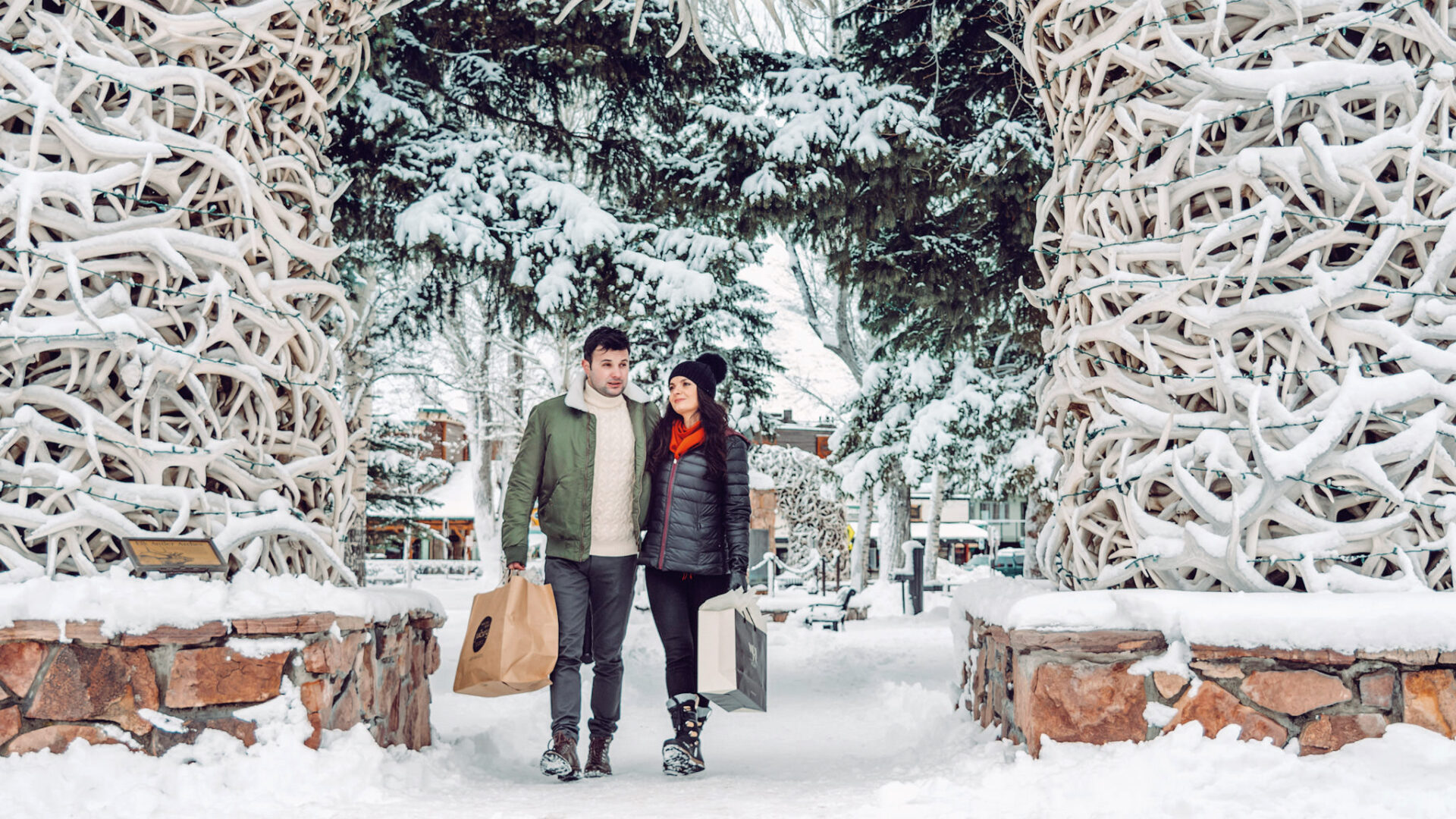 Winter-clad couple returns to their hotel with shopping bags, enjoying the awesome snowy view.