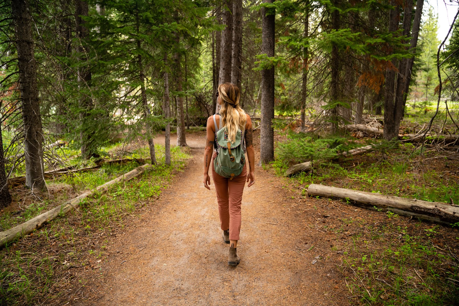 A girl with a shoulder bag strolls in the forest, admiring the beauty of towering trees.
