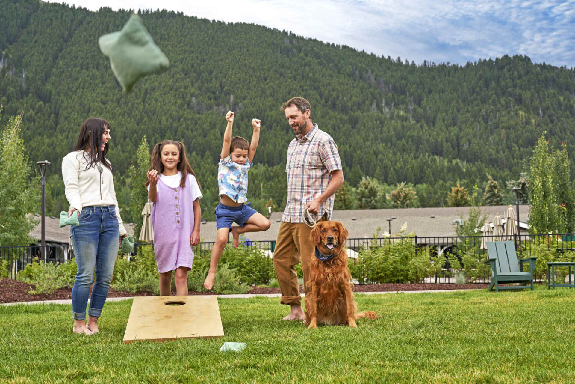 Family cherishes joyful moments in a grassy land, surrounded by lush greenery and mountains.