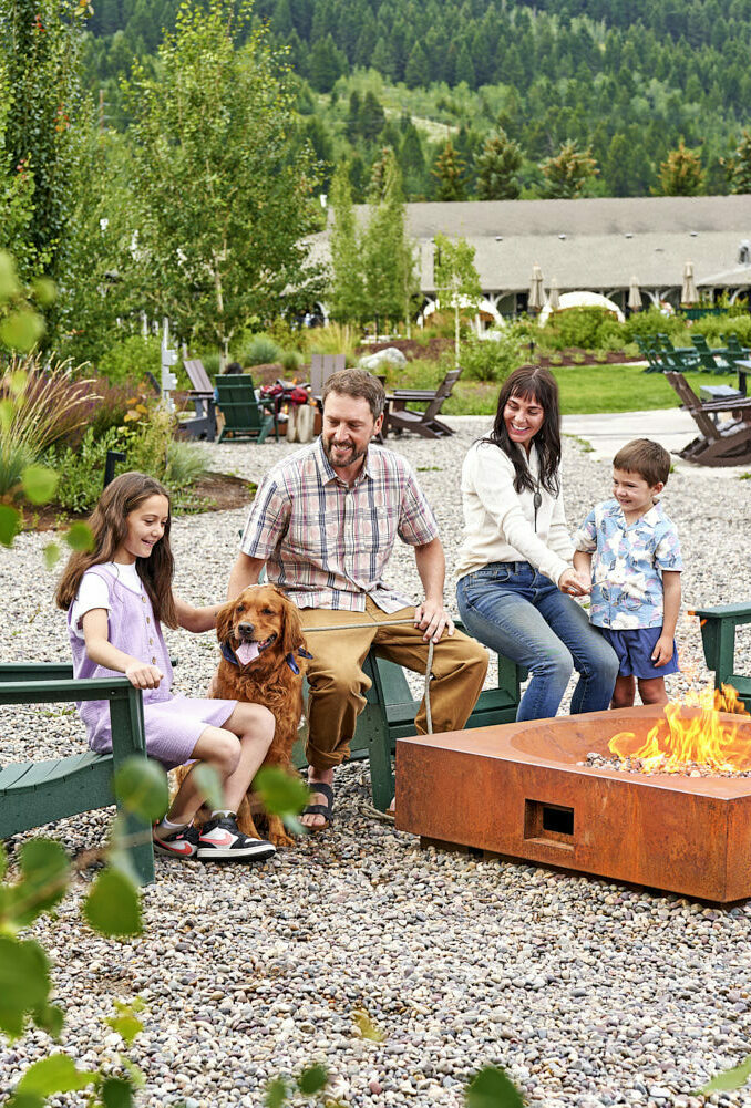 Family cherishing moments by the bonfire, surrounded by a scenic green plant-filled view.