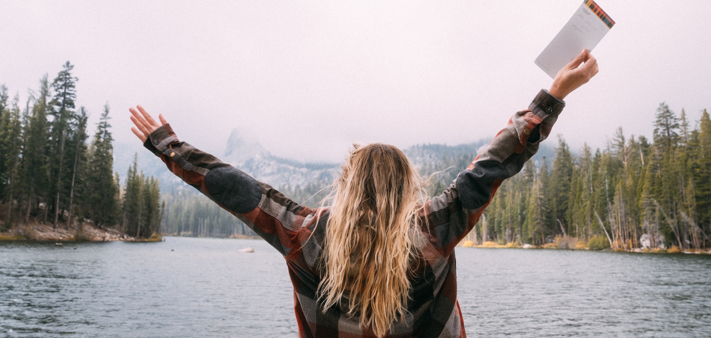 A woman raises her arms in front of a mountain lake near our Mammoth Lakes hotel