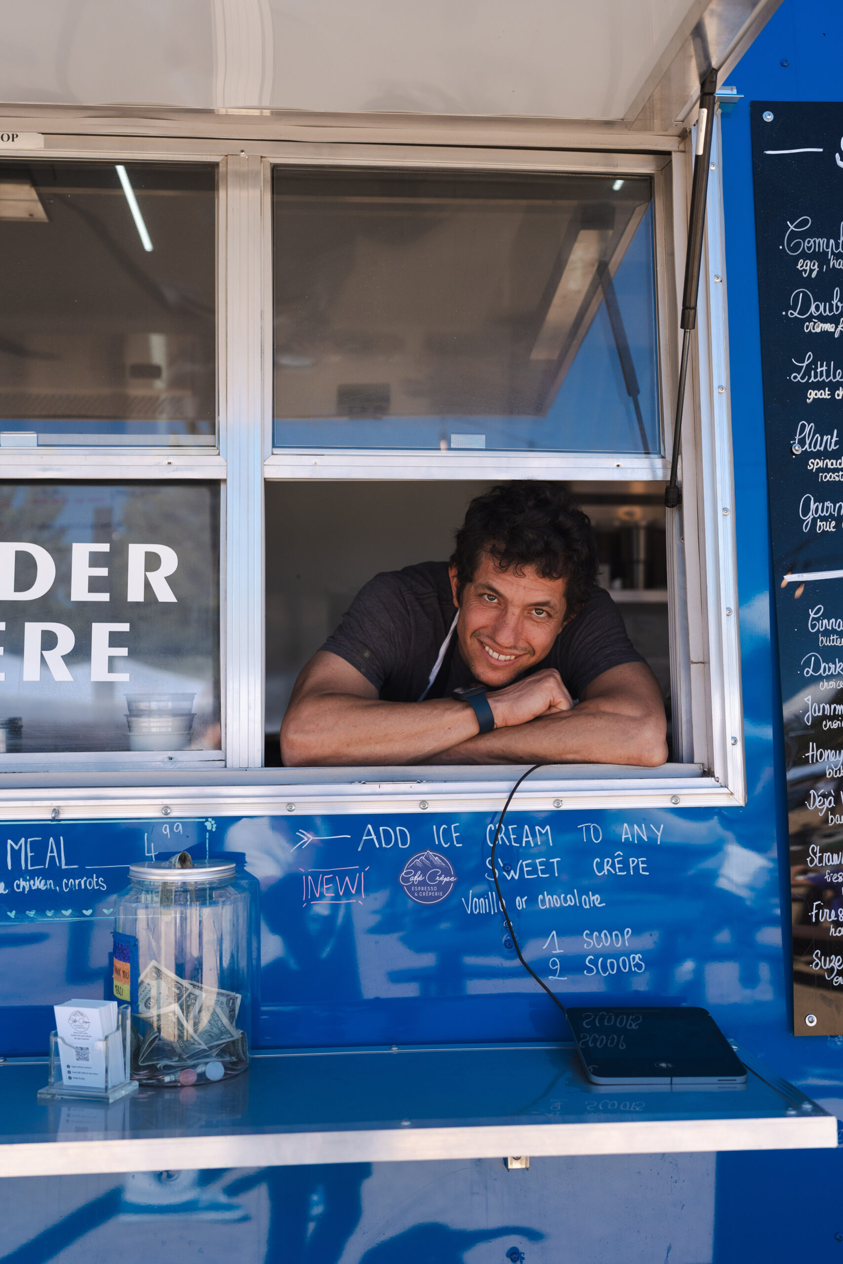 A man at the food truck window awaits his customer with a welcoming smile.
