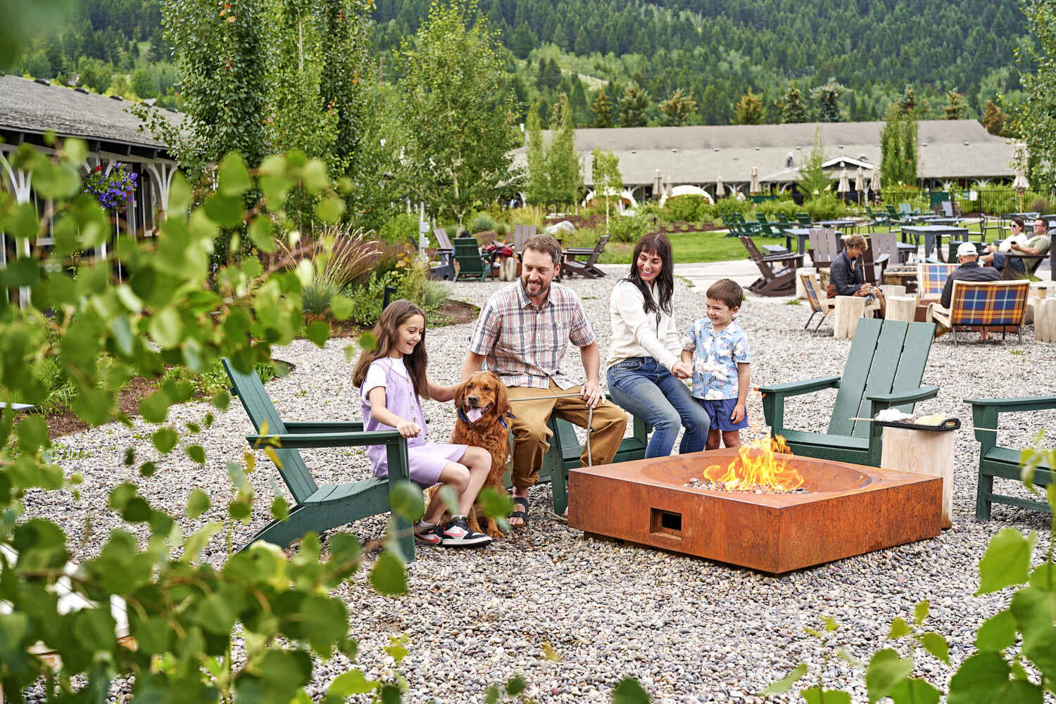 Family relishing memorable moments by the bonfire, surrounded by a scenic view of green plants.